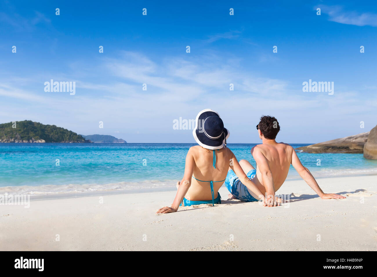 Happy young couple sitting together on paradise beach with clear turquoise sea water Stock Photo