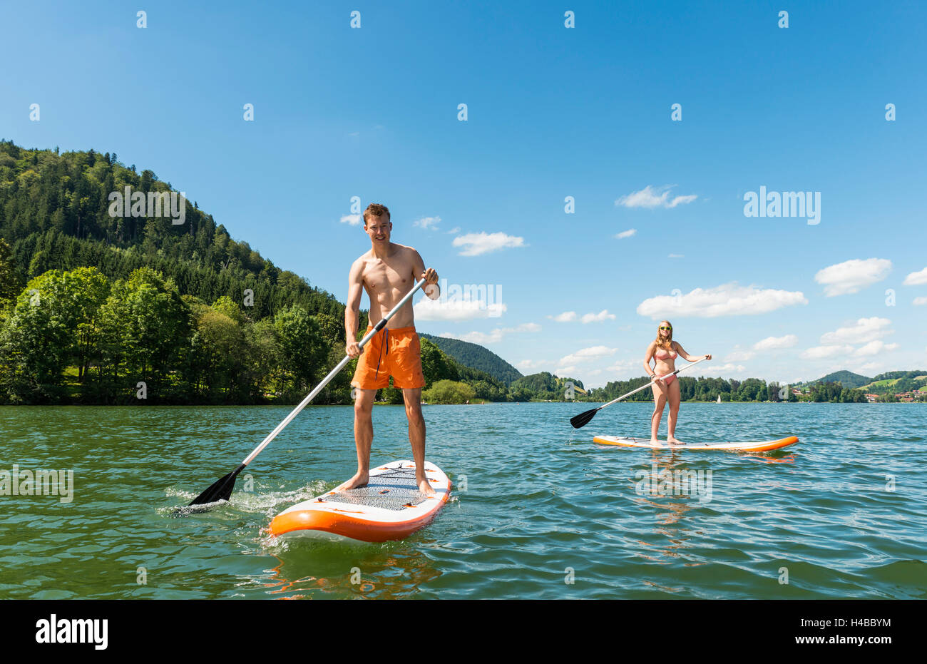 Young man and woman on paddle boards, using standup paddles, Lake