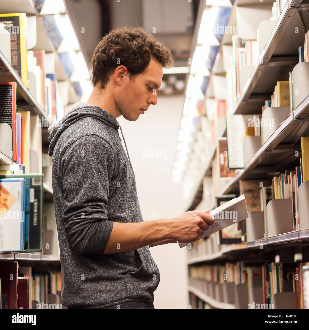 Student reading a book between library shelves, high school Stock Photo
