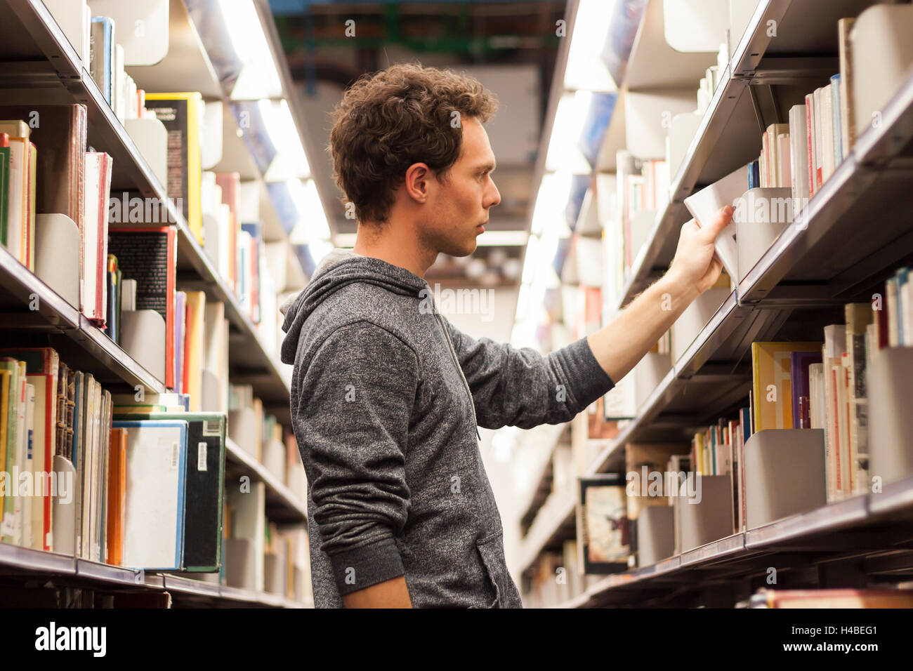 Young male student selecting a book from a library shelf, high school Stock Photo