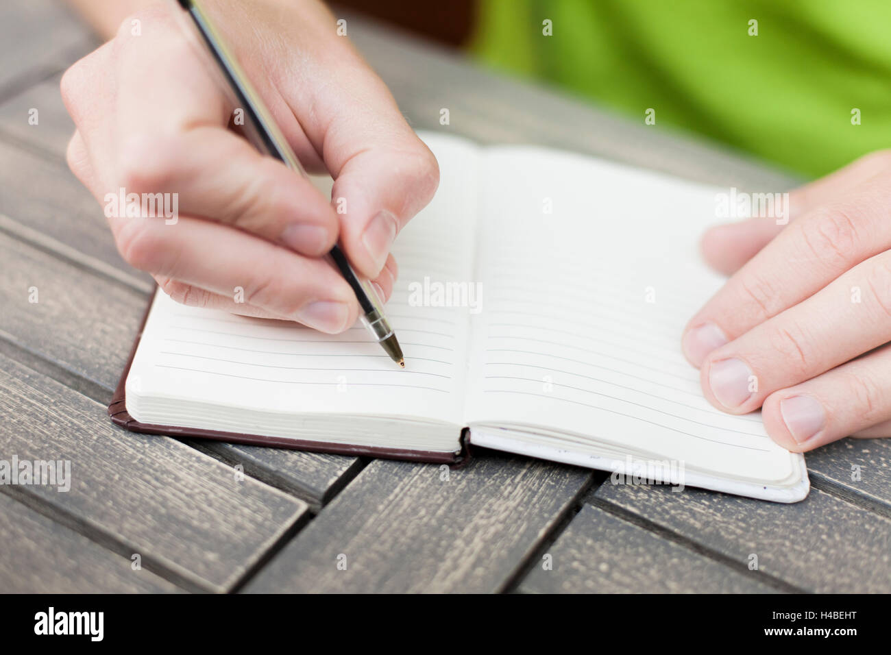Young man writing notes on a notebook with a pen, close-up view of hands Stock Photo