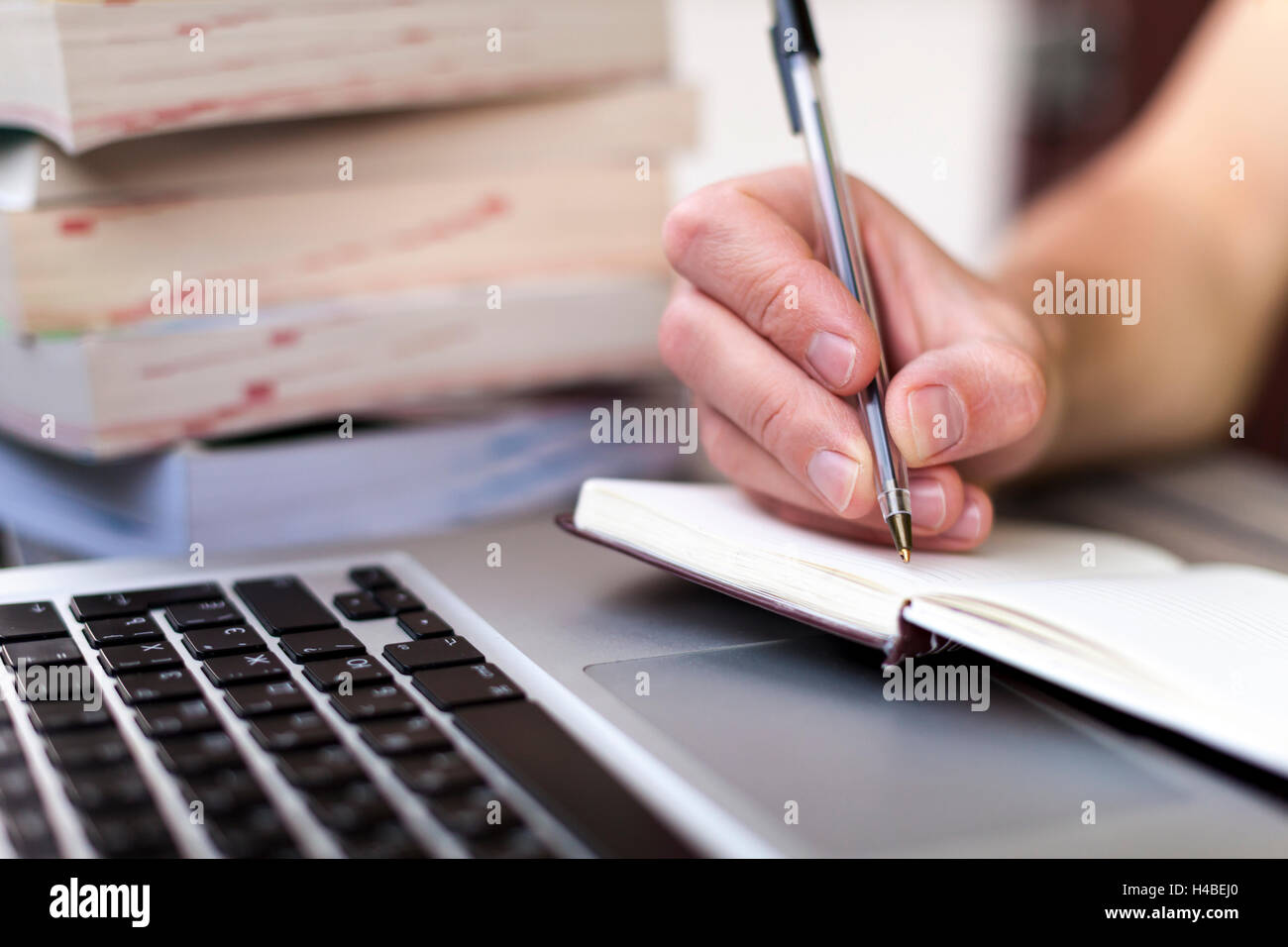 Young traveler writing down journey stories in a notebook with a laptop and books in the background Stock Photo