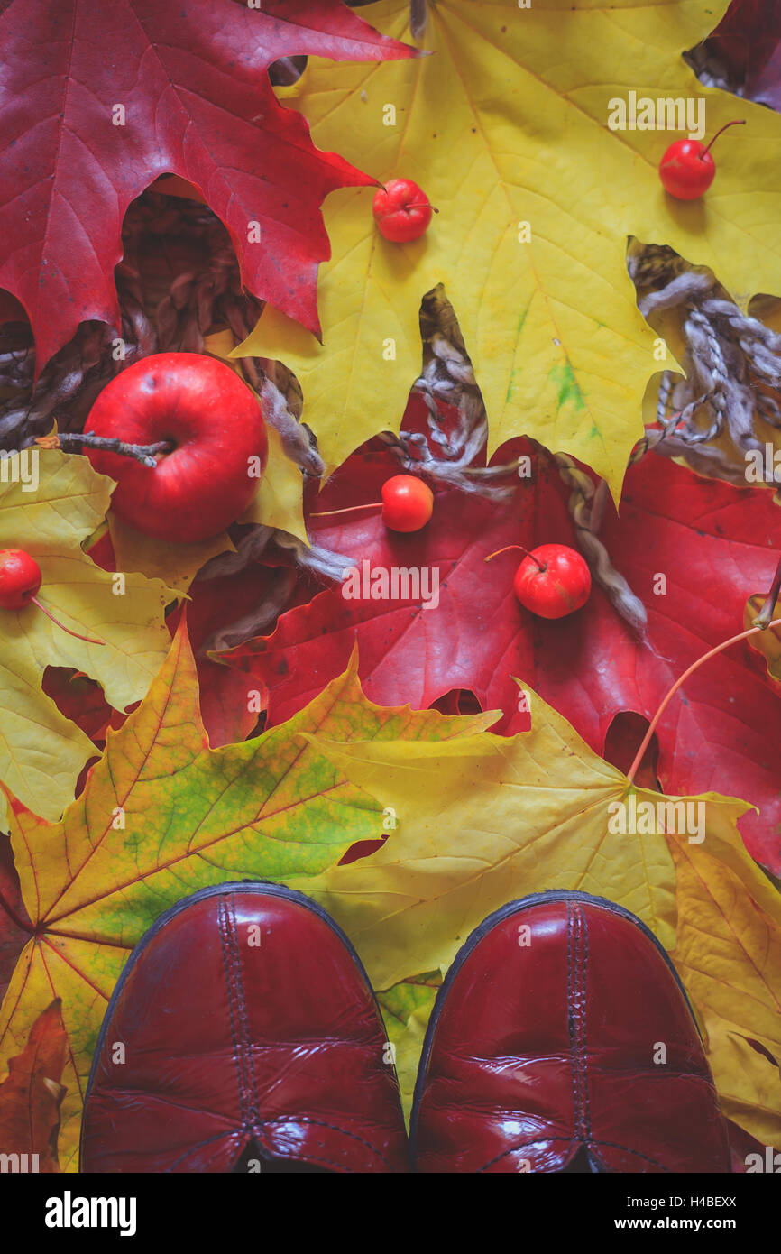 Still life autumn decoration with red shoes, colorful dry leaves woolen scarves and small red apples Stock Photo