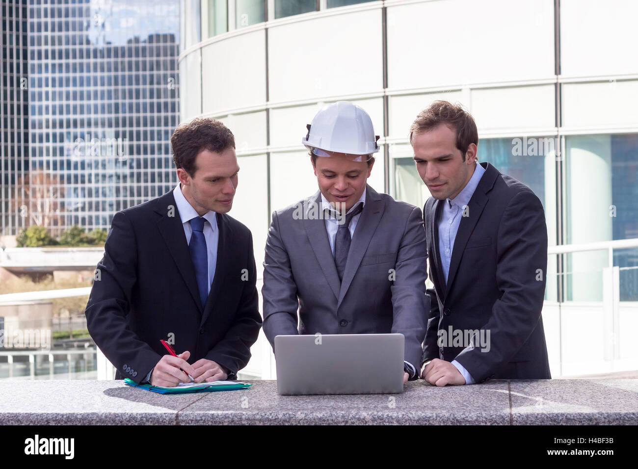 Business team with architect and engineer analyzing project on laptop with office buildings in background Stock Photo
