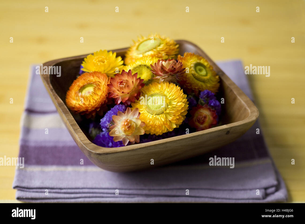Yellow and red straw flowers in wooden peel, mauve napkin, Stock Photo