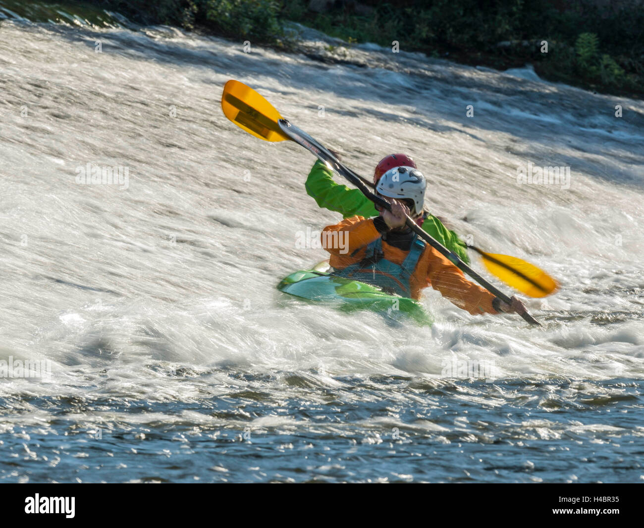 Two male adults White Water Kayaking along a River Exe Weir on a bright
