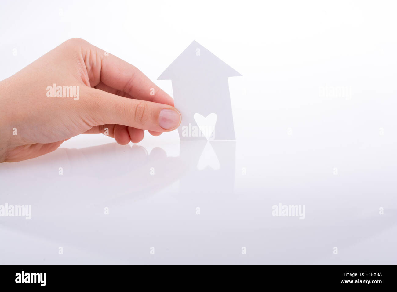 Hand holding a paper house with a heart carved in it on a white ...