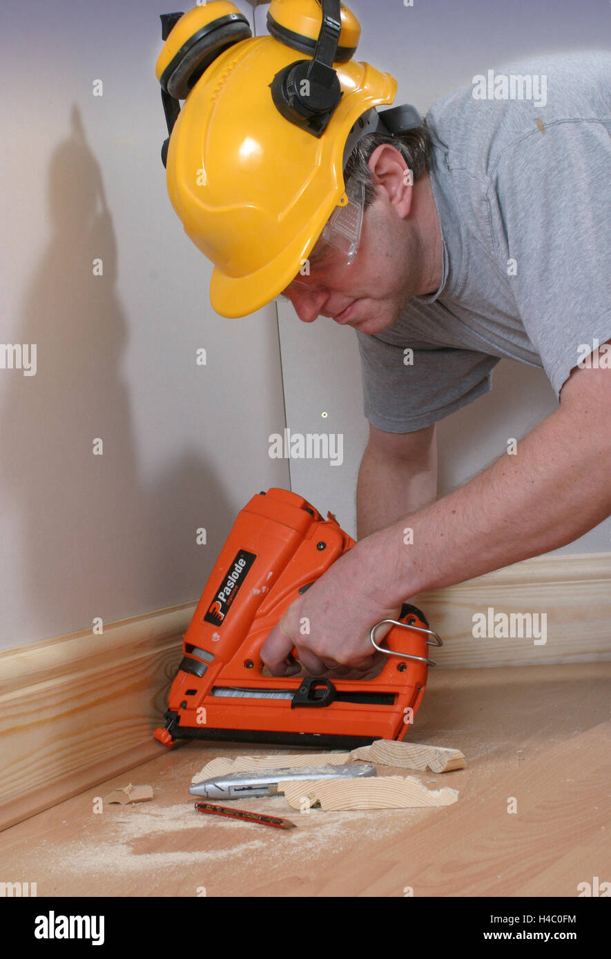 A carpenter uses a gas powered nail gun to fix trim around a new timber laminate floor. Stock Photo