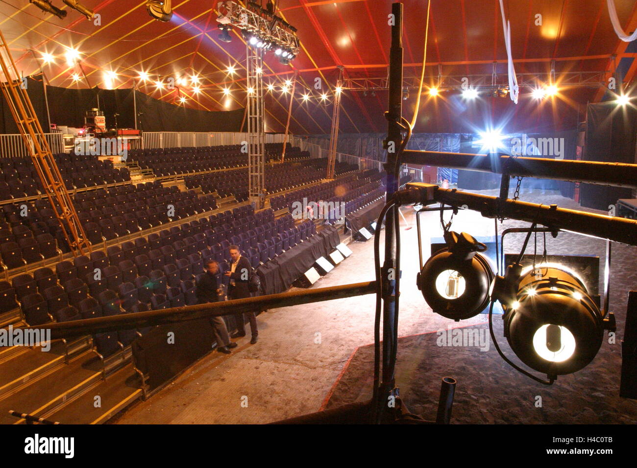 Interior of a newly erected circus-style tent showing sand performance area, tiered seating and spotlights in the foreground Stock Photo