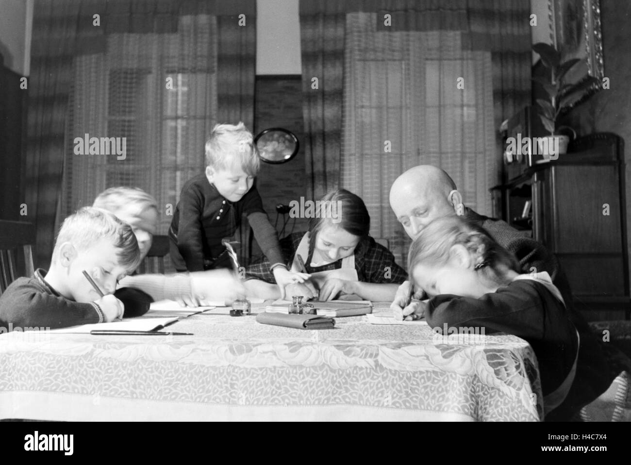 Mitglieder einer kinderreichen Familie bei den Hausaufgaben, Deutsches Reich 1930er Jahre. Members of a extended family doing the homework, Germany 1930s Stock Photo