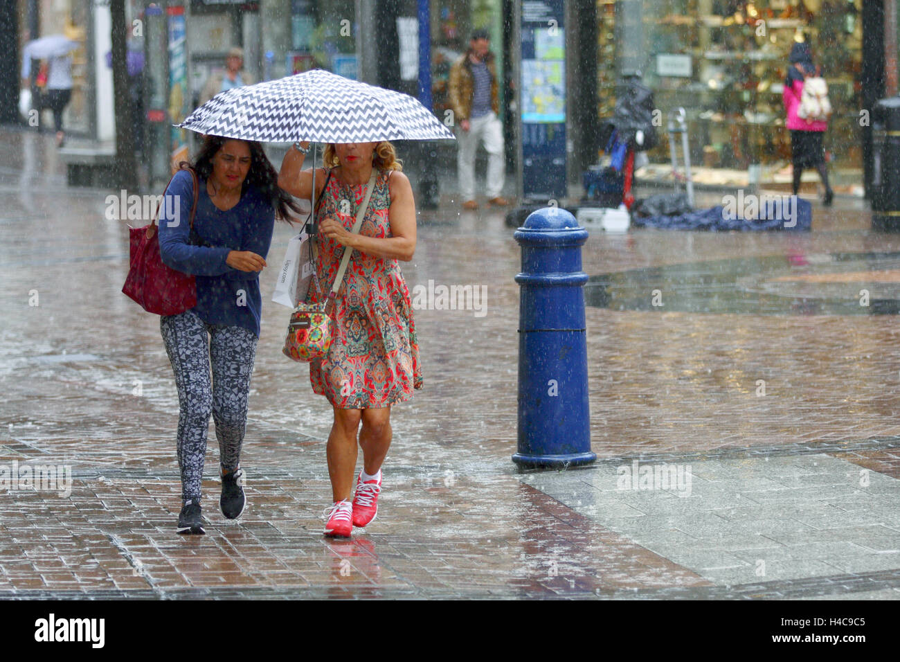 Two females caught in a sudden shower of rain try to stay dry under an umbrella in Kingston, Surrey, England. Stock Photo
