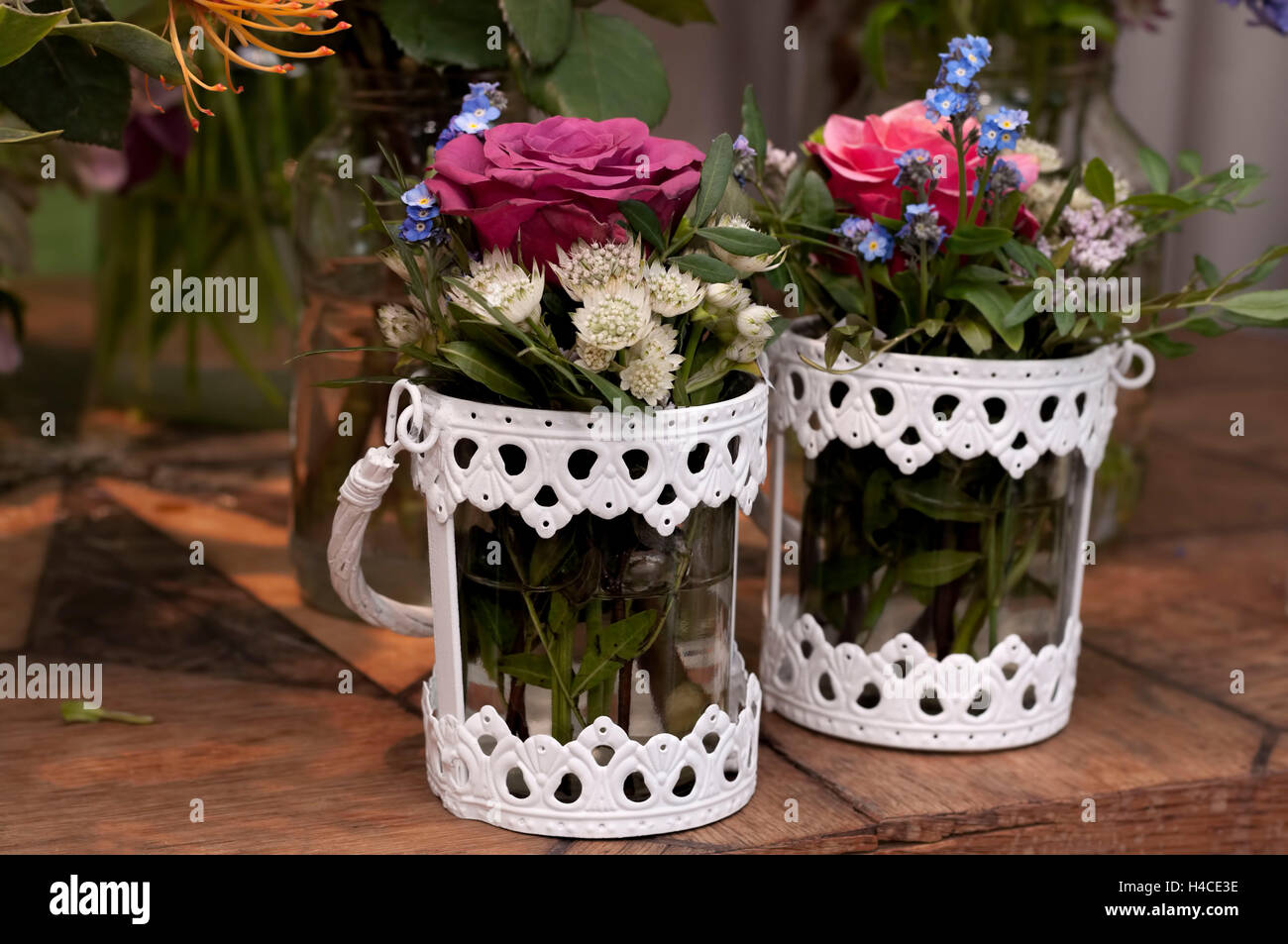 Two white vases of glass and metal with small flower bunches on a wooden board, in the background other cut flowers Stock Photo