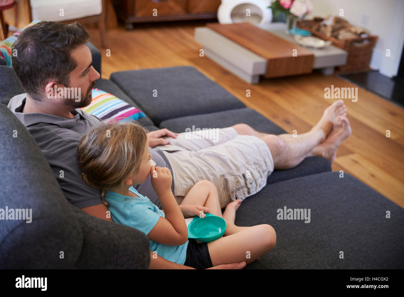 Father And Daughter Sitting On Sofa Watching TV Together Stock Photo