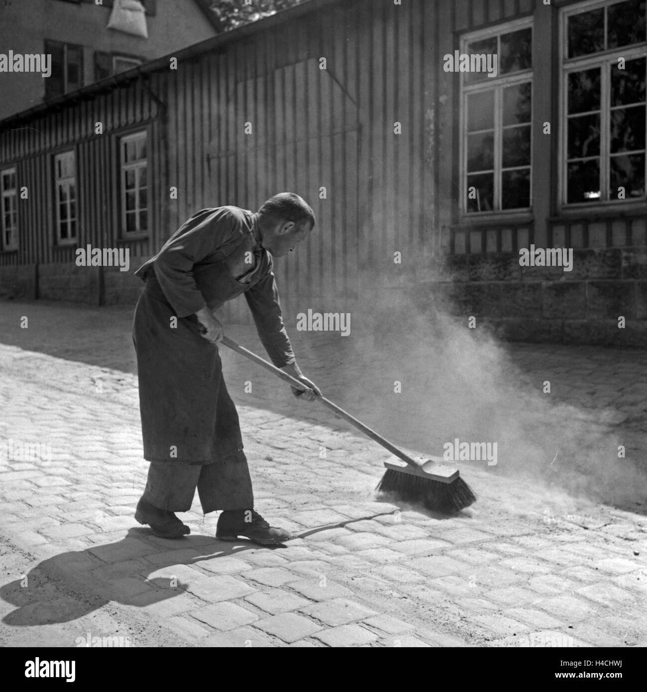 Ein Mann in Freudenstadt im Schwarzwald fegt seinen Hof, Deutschland 1930er Jahre. A man sweeping a courtyard at Freudenstadt in Black Forest, Germany 1930s. Stock Photo