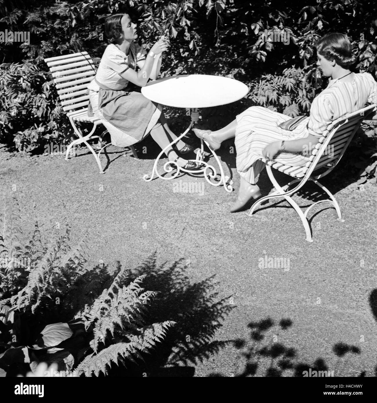 Zwei Frauen sitzen in der prallen Sonne an einem Gartentisch, Deutschland 1930er JAhre. Two women sitting on garden furniture in the sun, Germany 1930s. Stock Photo