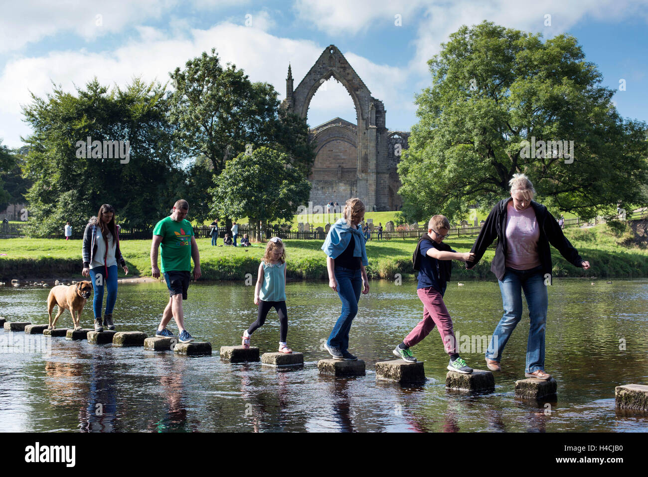 Members of the public cross the River Wharfe along with their dog, whilst enjoying the sunshine, at Bolton Abbey, in Wharfedale, Stock Photo