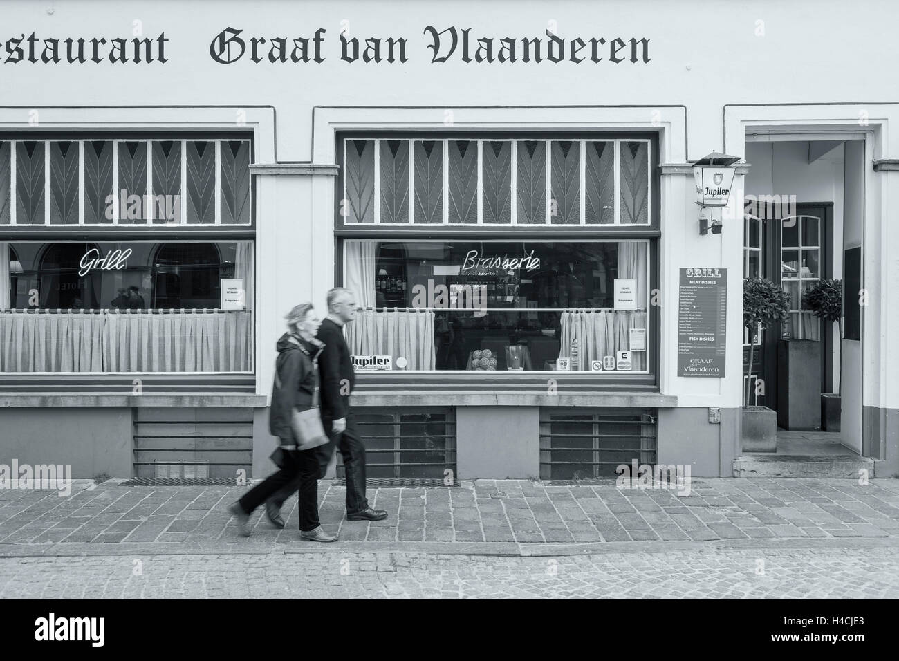 Belgium, West Flanders, Bruges, walking couple (middle-aged) in step in front of a restaurant Stock Photo