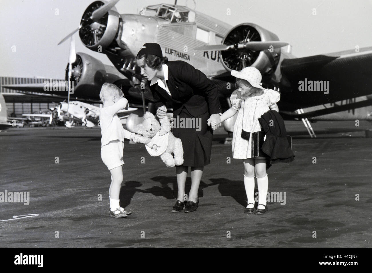 Eine Stewardess fhrt zwei Kinder ber das Flugfeld zum Flugzeug, Deutschland 1930er Jahre. Stewardess leading two children over the airfield to the plane, Germany 1930s Stock Photo