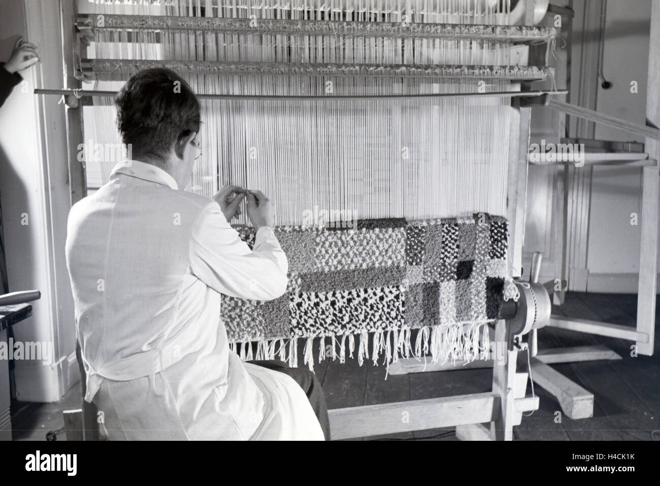 Ein Mitarbeiter einer Textilfirma in Krefeld knüpft einen teppich an einem großen hölzernen Webrahmen, Deutschland 1930er Jahre. An employee in a textile company in Krefeld weaving a rug on a big wooden loom, Germany 1930s Stock Photo