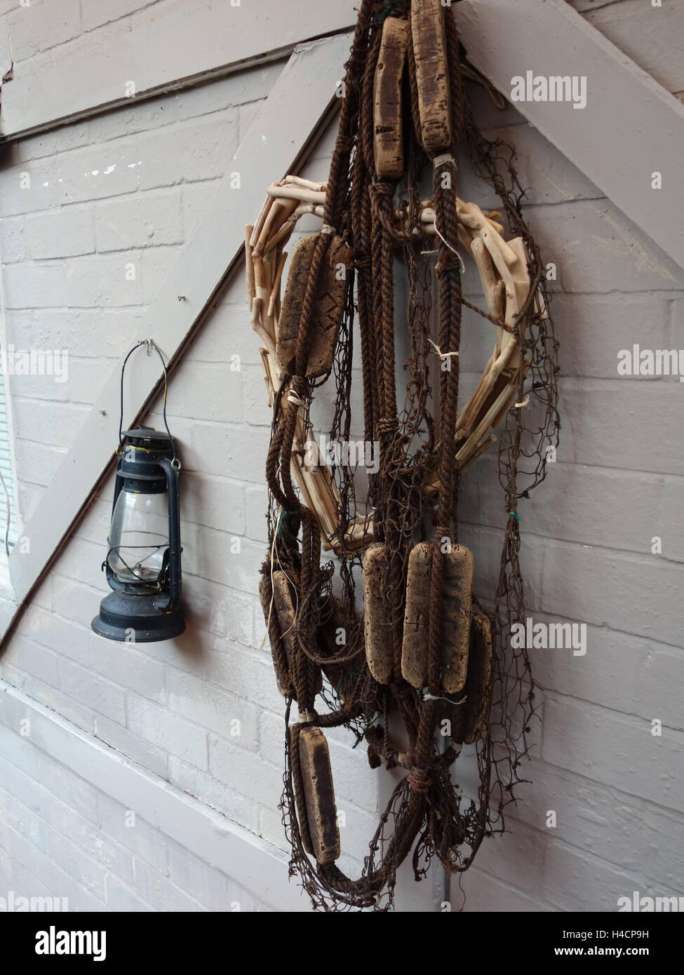 An old fishing net hanging next to a lamp on an old wall. Stock Photo