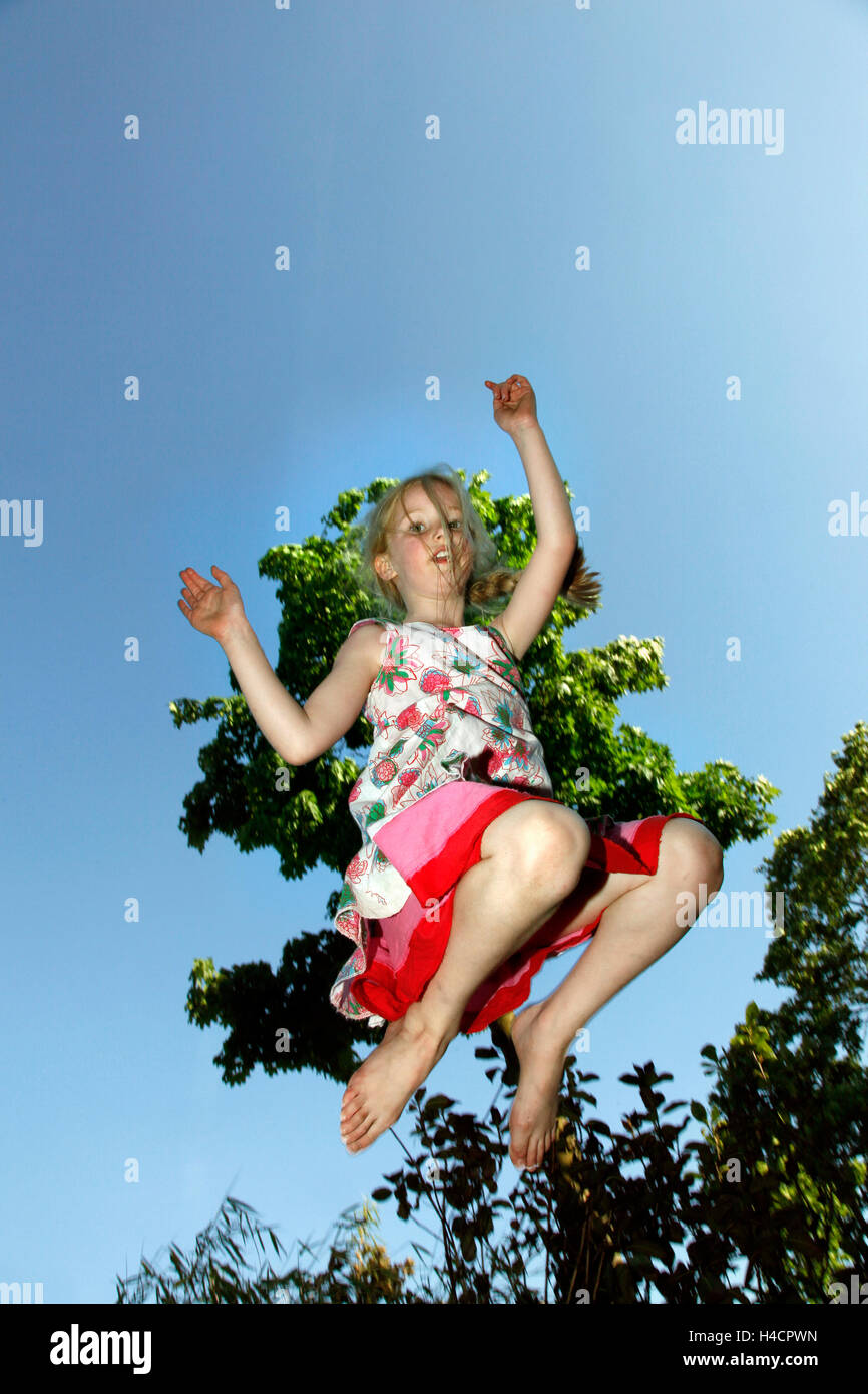 young blond girl jumps against blue sky and tree Stock Photo - Alamy