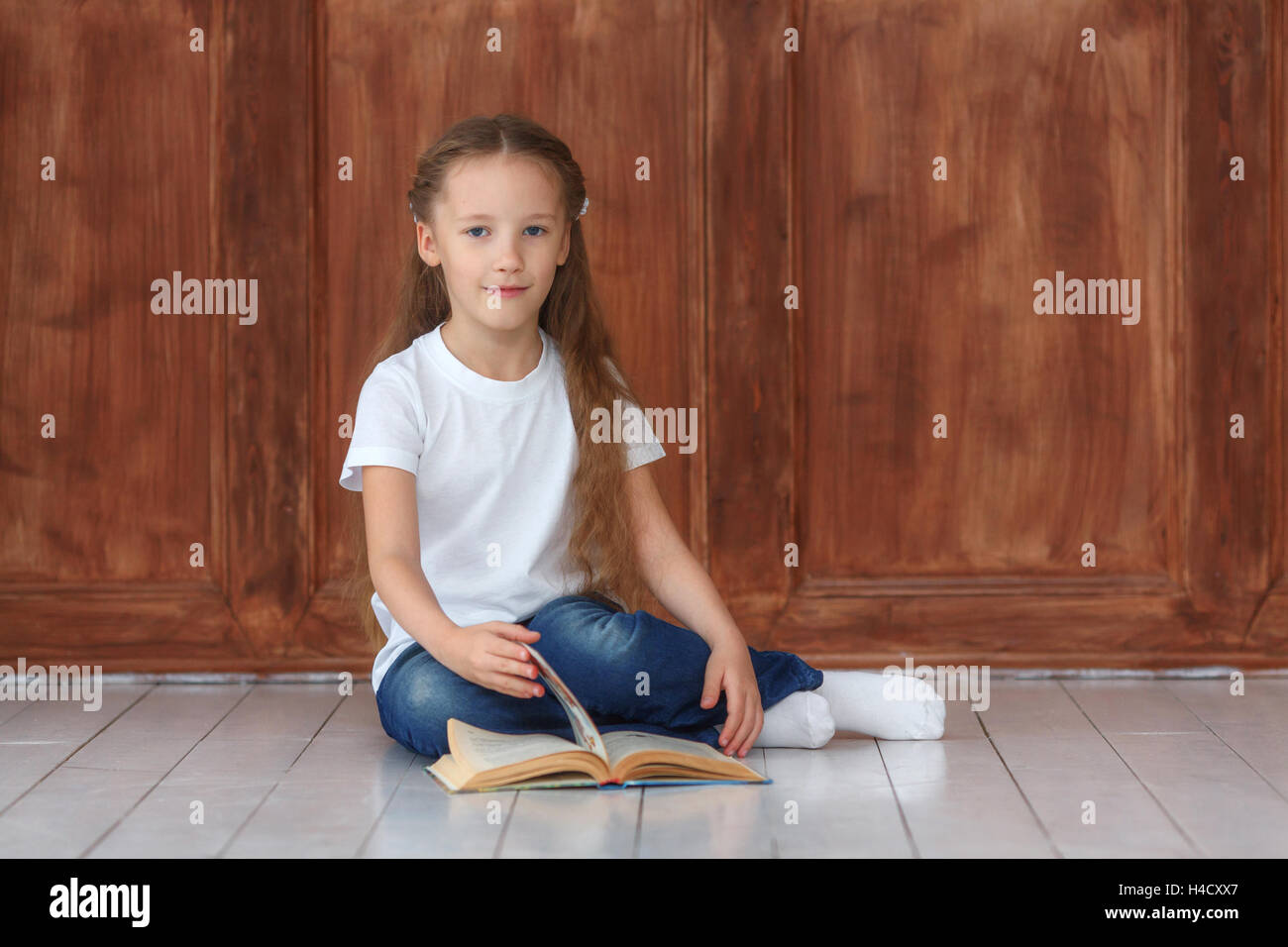 Little girl sitting on the wooden floor and reading book Stock Photo ...