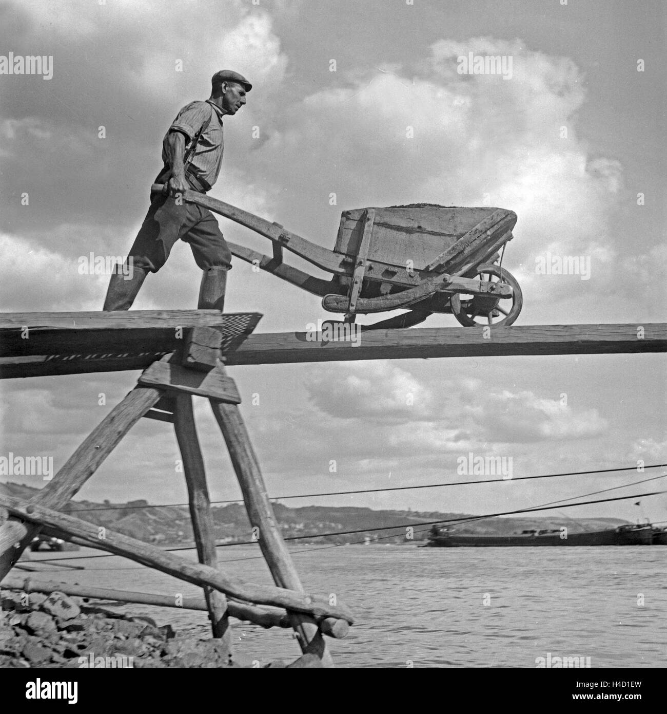 Ein Arbeiter in einem Basaltwerk am Rhein mit seiner Schubkarre, Deutschland 1930er Jahre. A worker of a basalt factor at river Rhine with his barrow, Germany 1930s. Stock Photo