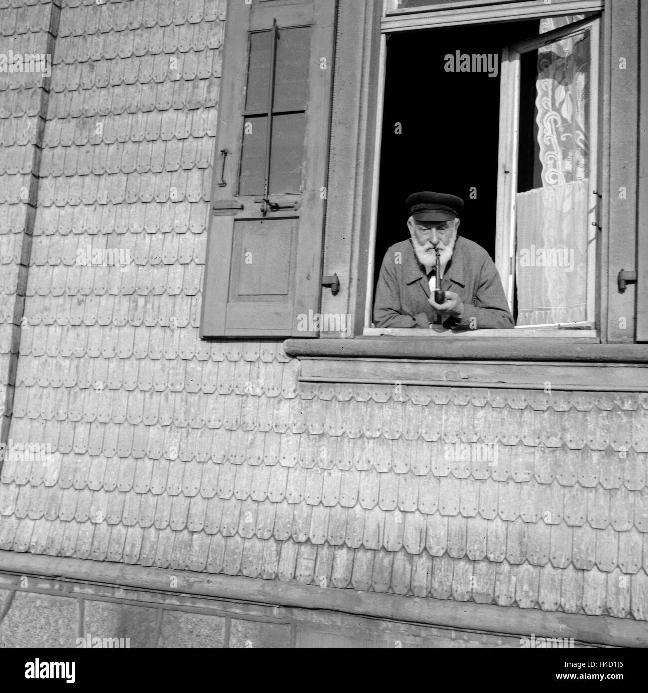 Ein Mann raucht seine Pfeife und schaut dabei aus dem Fenster, Deutschland 1930er Jahre. A man smoking his pipe while watching out of the window, Germany 1930s. Stock Photo