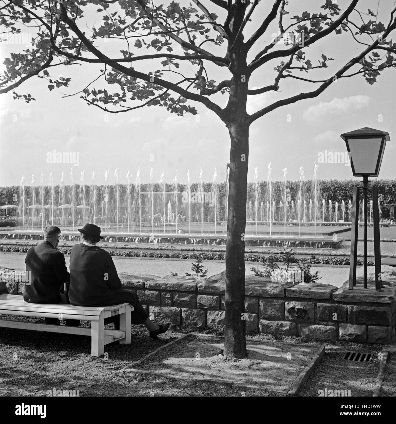 Ein Paar sitzt auf einer Bank im Grugapark in Essen und schaut sich die Wasserspiele an, Deutschland 1930er Jahre. A couple sitting on a bench at Essen Grugapark gardens watching trick fountains, Germany 1930s. Stock Photo