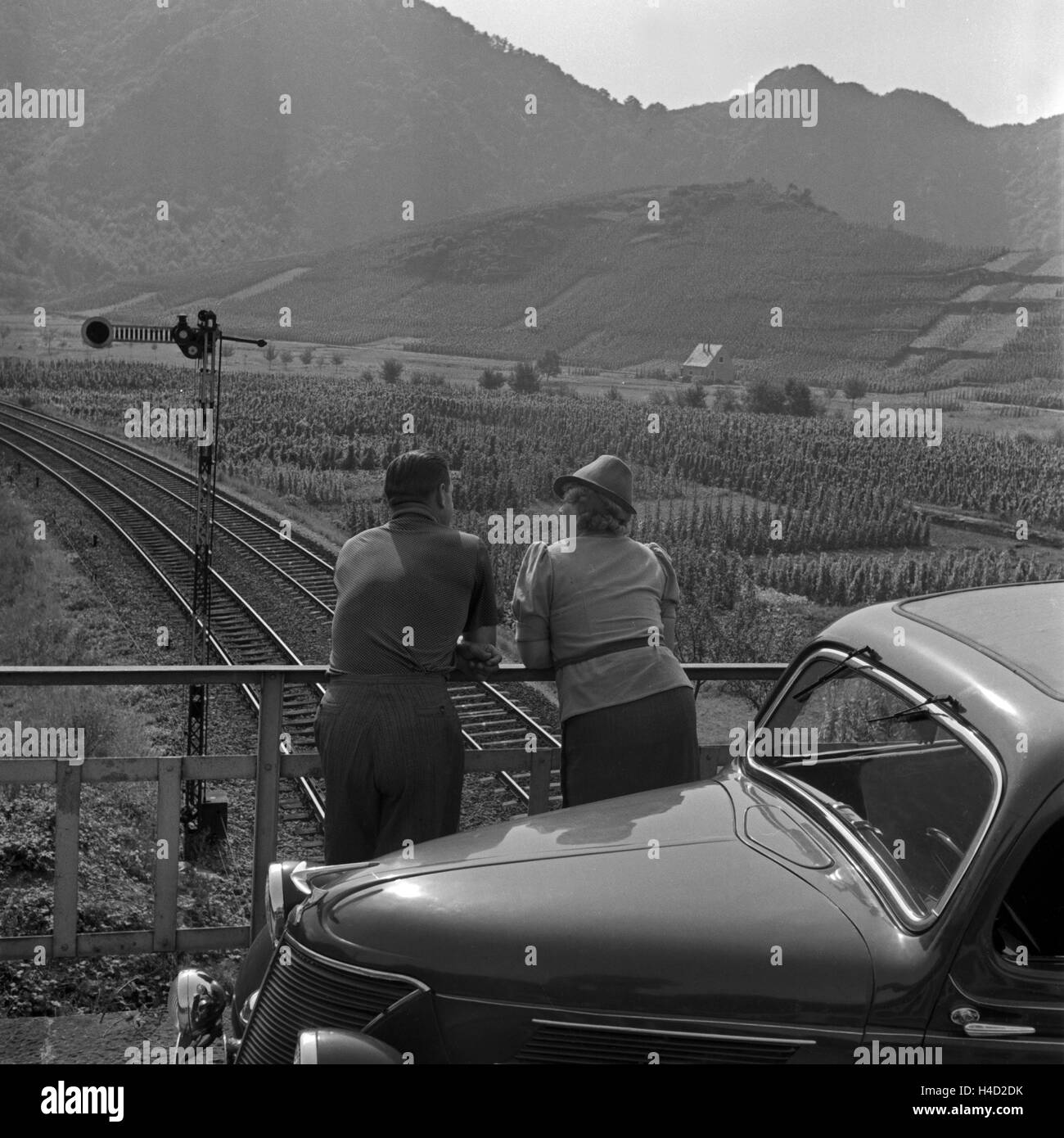 Ein Mann und eine Frau stehen mit ihrem Ford Eifel auf einer Brücke über eine Eisenbahnstrecke im Ahrtal, Deutschland 1930er Jahre. A man and a woman with their Ford model Eifel standing on a bridge over a railway track at the valley of river Ahr, Germany 1930s. Stock Photo