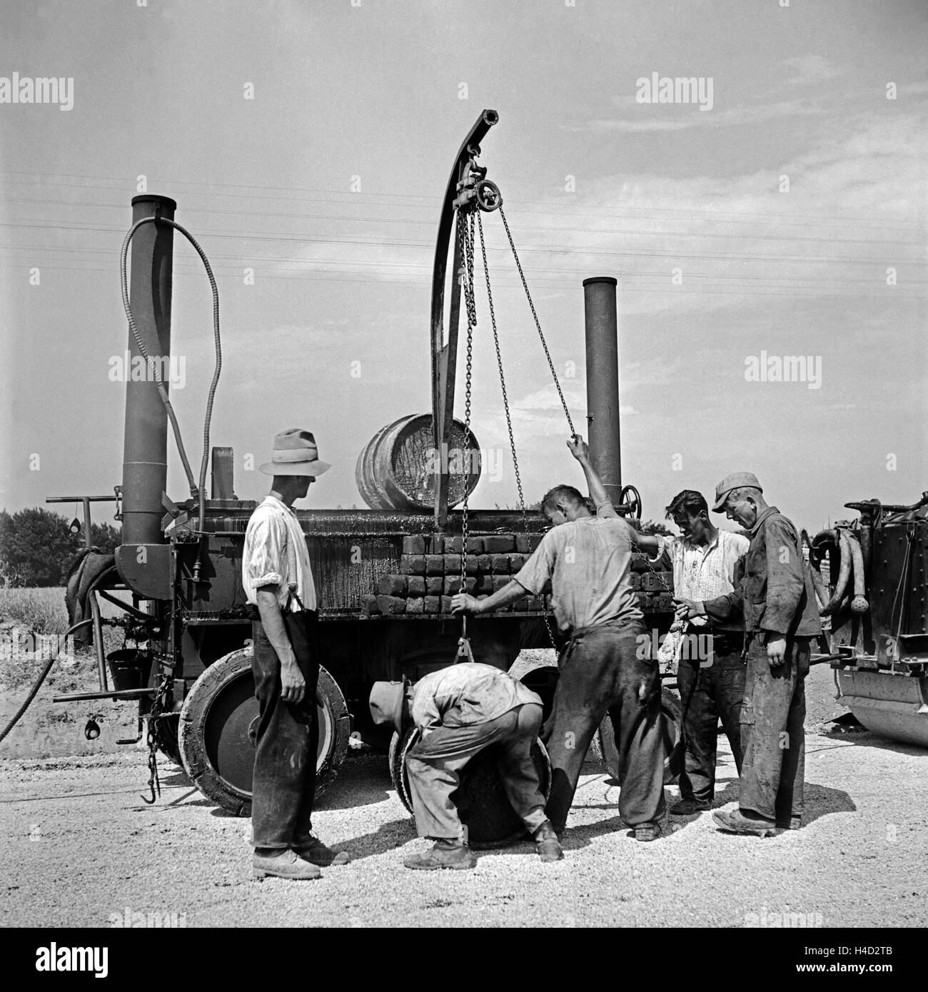Bauarbeiter an einer Teermaschine in Burghausen, Deutschland 1930er Jahre. Construction workers working with their ropemaker's stove at a street in the ciyt of Burghausen, Germany 1930s. Stock Photo