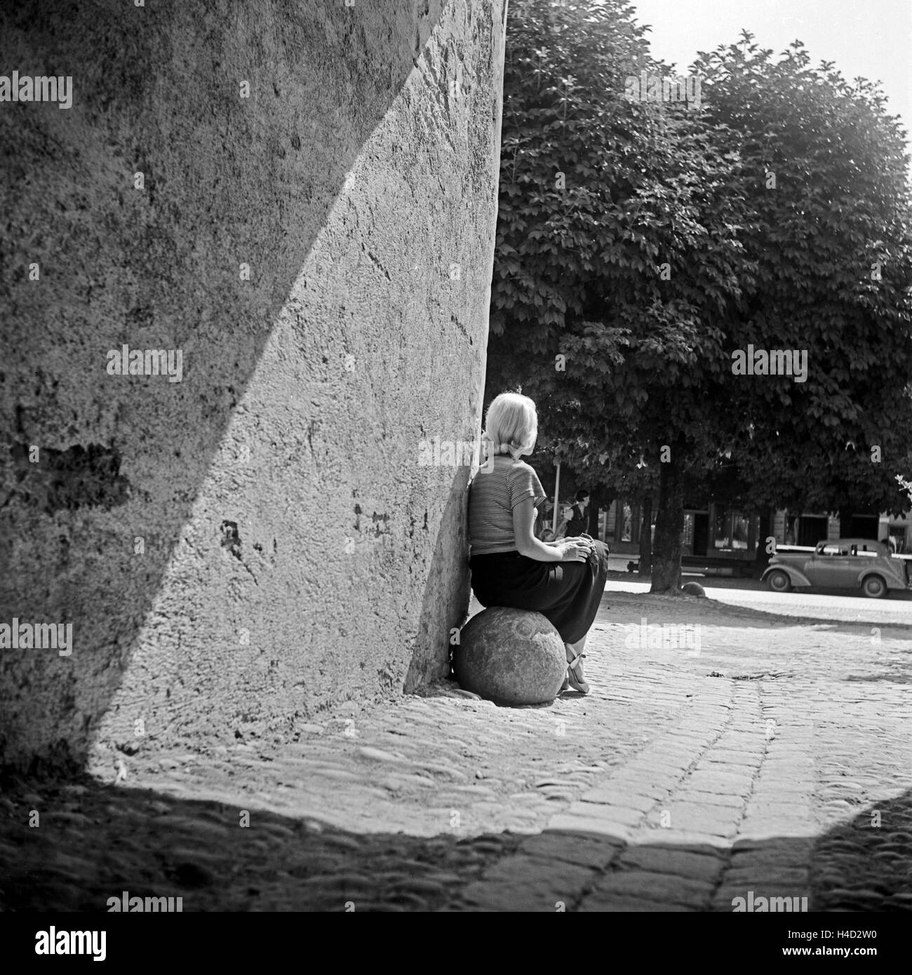 Eine junge Frau sitzt auf einer Steinkugel an einem Stadttor in Passau, Deutschland 1930er Jahre. A young woman sitting on a stone ball at a medieval city gate, Germany 1930s. Stock Photo