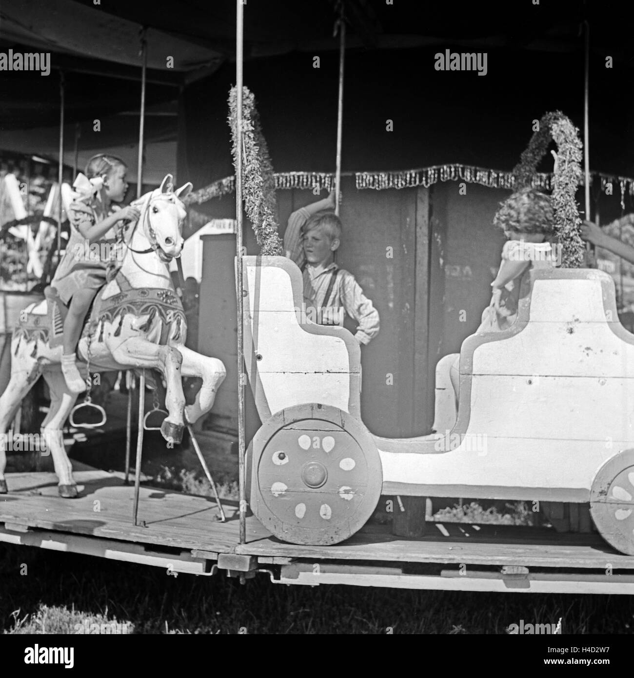 Kinder auf einem Karussell auf einem Volksfest, Deutschland 1930er Jahre. Children on a carousel at an annual fair, Germany 1930s. Stock Photo
