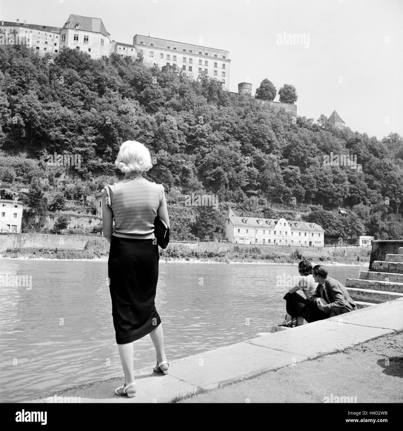 Eine junge Frau steht an der Donau mit Blick auf die Veste Oberhaus, Deutschland 1930er Jahre. A young woman standing on the shore of river Danube watching Oberhaus castle at Passau, Germany 1930s. Stock Photo