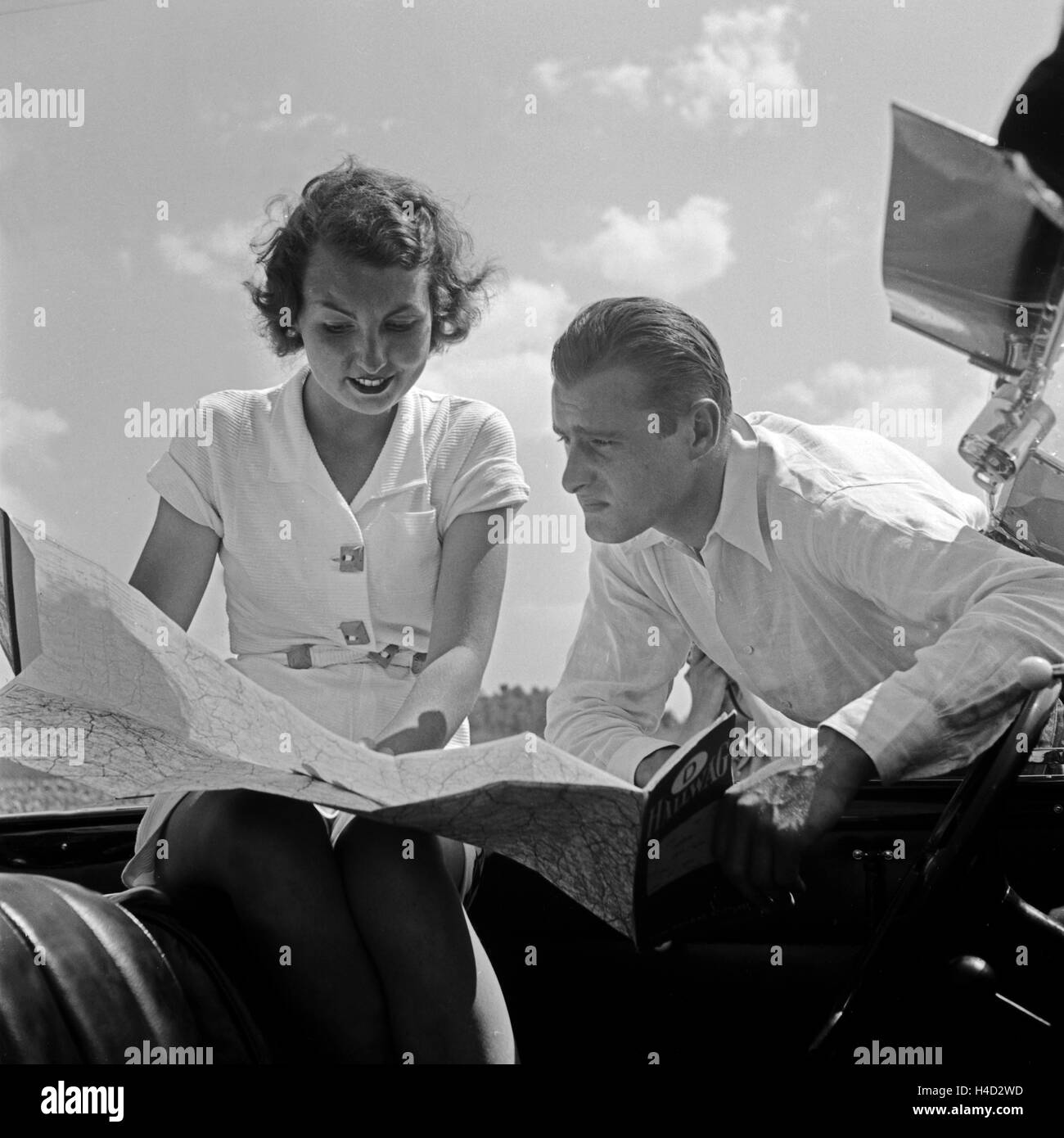 Ein junger Mann und eine junge Frau ziehen bei einer Autofahrt die Hallwag Straßenkarte zu Rate, Deutschland 1930er Jahre. A young couple using the Hallwag road map, Germany 1930s. Stock Photo