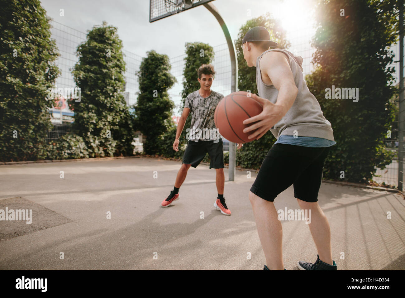 Shot of young man dribbling ball with friend blocking on basketball court. Friends playing basketball on outdoor court. Stock Photo
