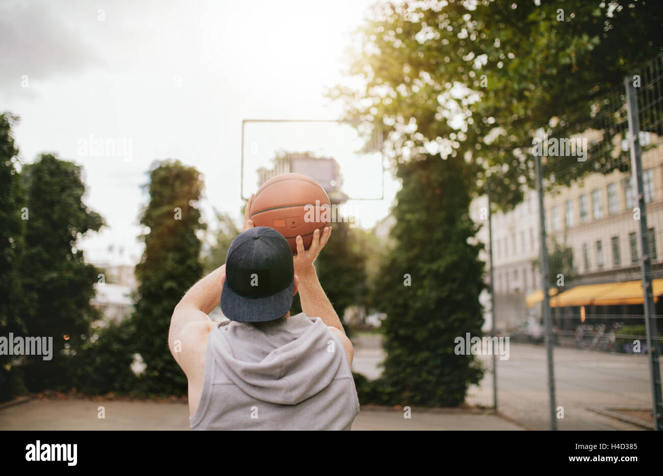 Rear view shot of a young guy playing basketball on outdoor court. Streetball player shoots basket. Stock Photo