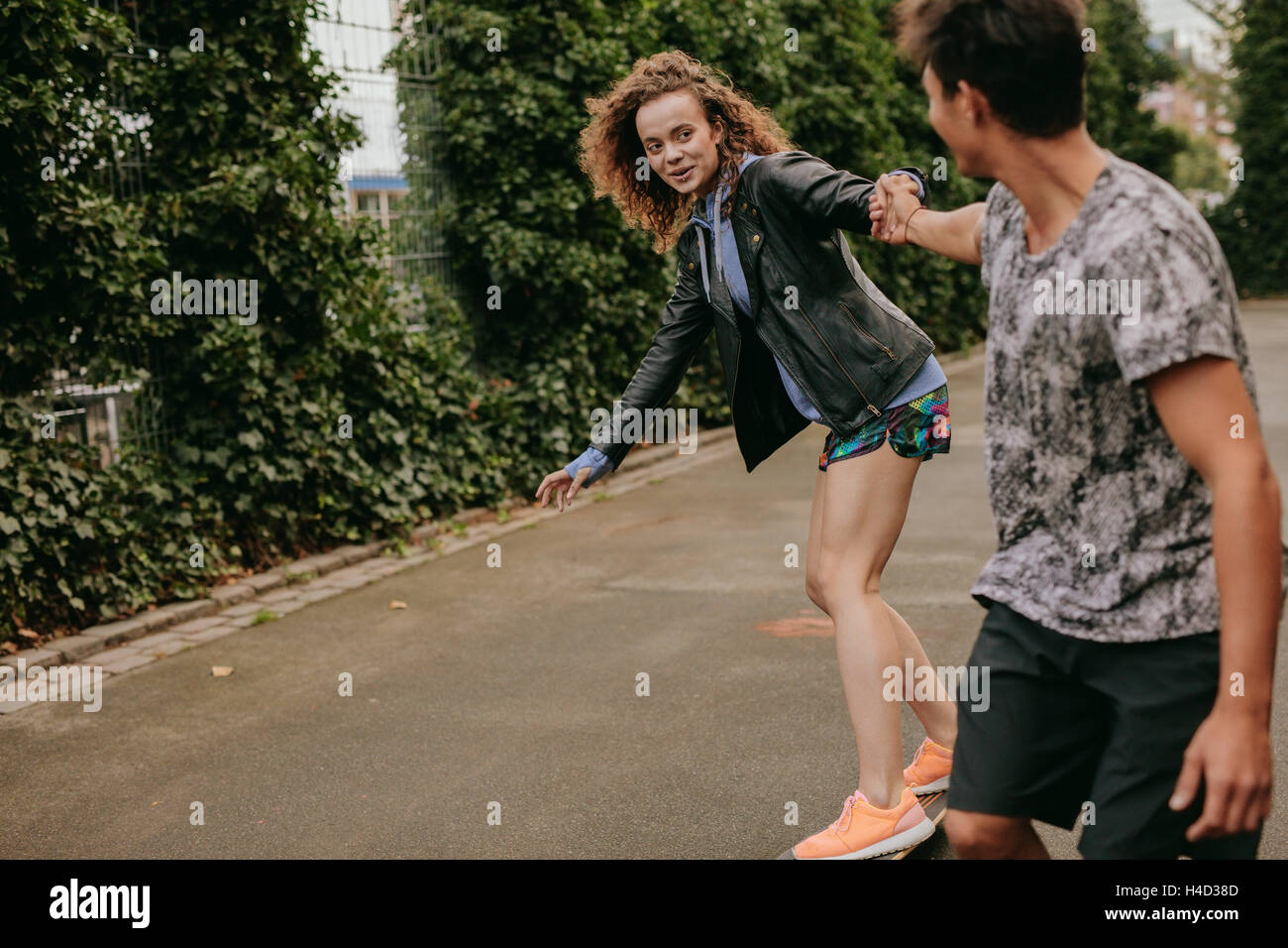 Teenage girl on a skateboard with support from her boyfriend. Woman skating on a basketball court with friend. Stock Photo