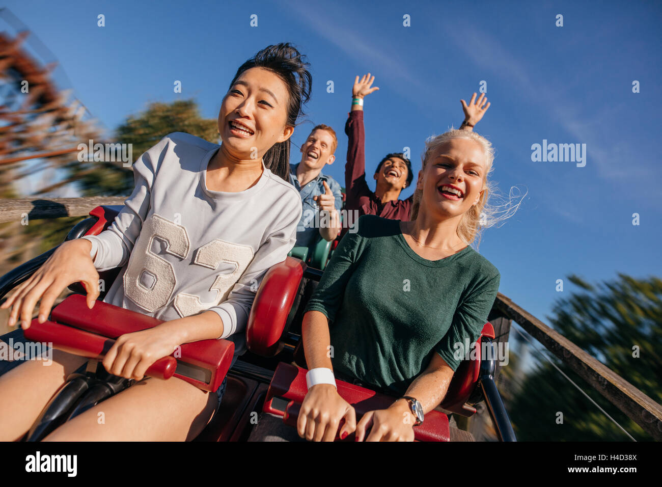 Young people on a thrilling roller coaster ride. Group of friends having fun at amusement park. Stock Photo