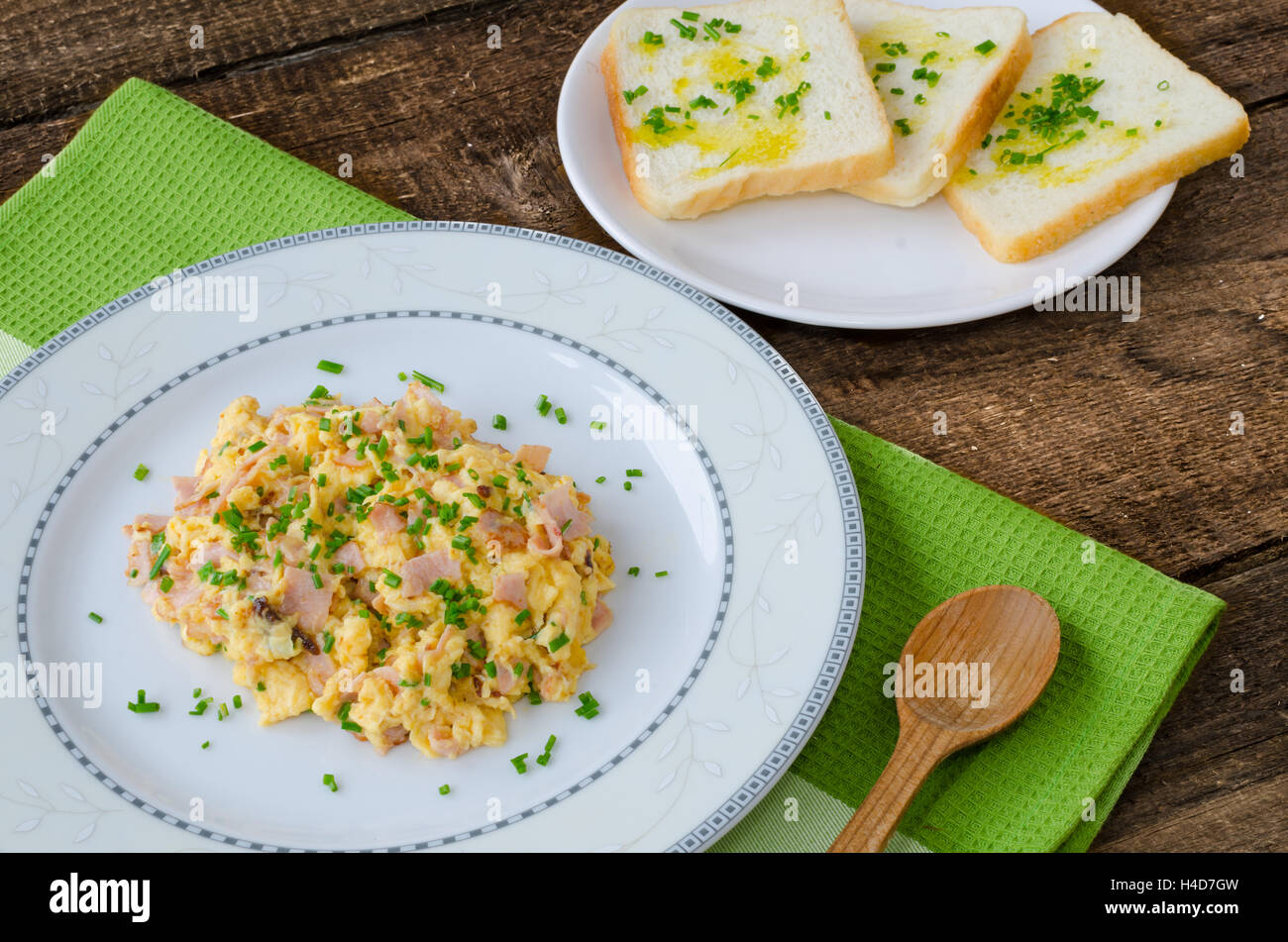 Scrambled eggs with chive and bacon, toast with herbs on wood table ...