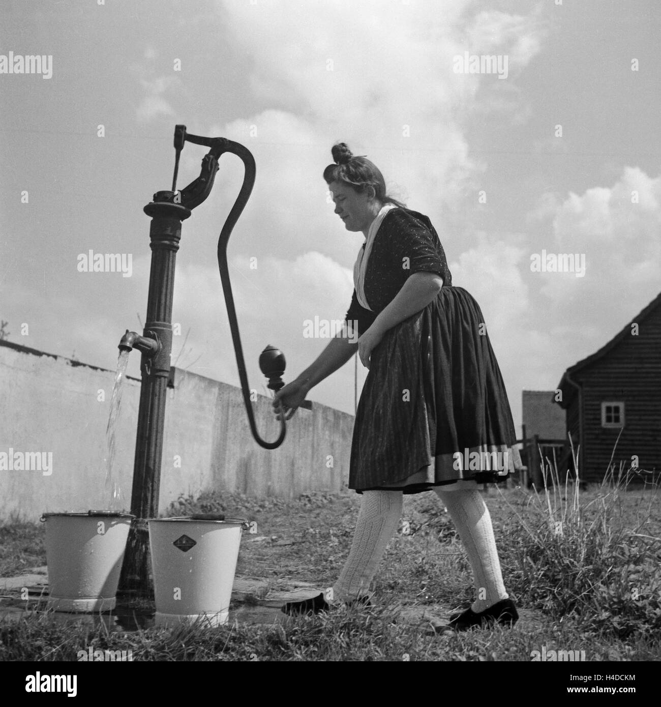 Eine Frau in der Tracht des Schwalm Eder Kreises holt Wasser am Pumpbrunnen, Deutschland 1930er Jahre. A woman wearing the array of the Schwalm Eder district pumping for water from a well, Germany 1930s. Stock Photo