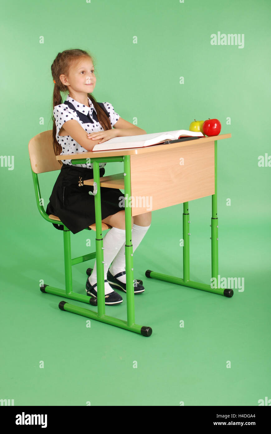 Girl in a school uniform sitting at a desk and reading a book isolated ...