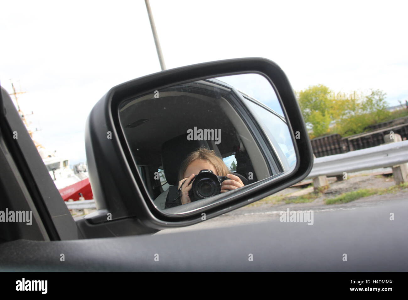 Little girl attempting to take a selfie in a side mirror of an automobile. Stock Photo