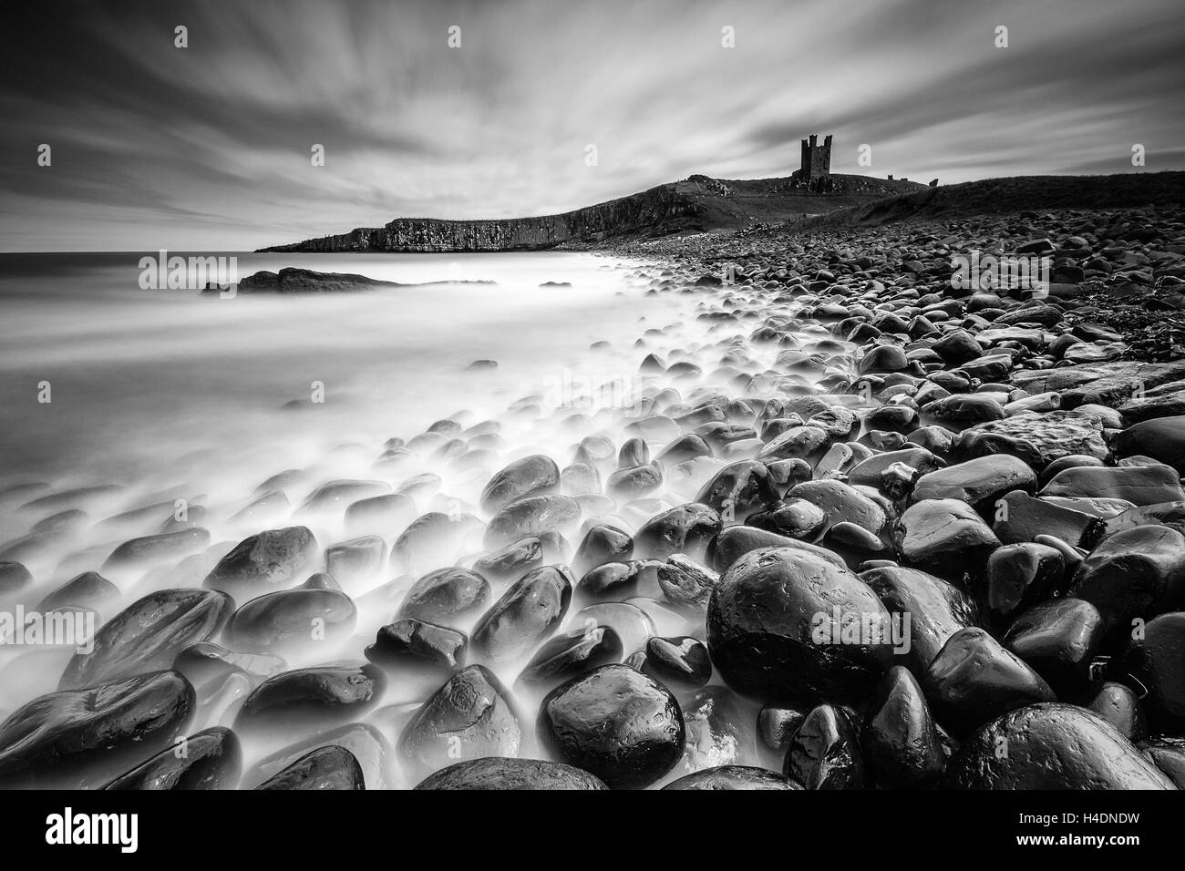The ruins of Dunstanburgh Castle at Embleton Bay in Northumberland, long exposure from the boulder field rocky shore line Stock Photo