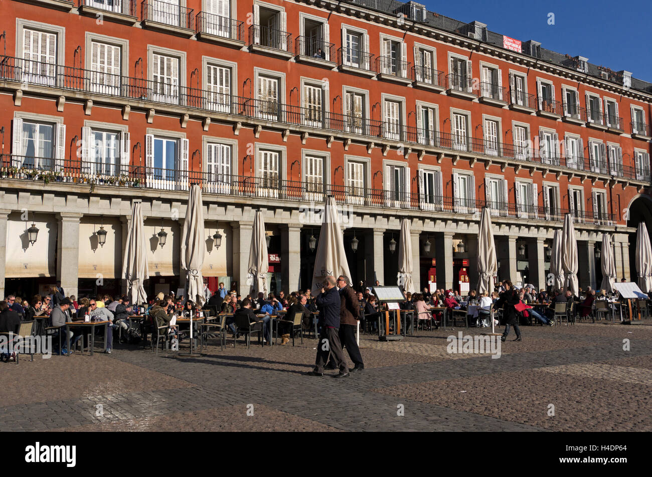 Plaza Mayor, visitors stroll around the plaza in late afternoon.  Tables and chairs filled with coffee or alcohol drinkers. Stock Photo