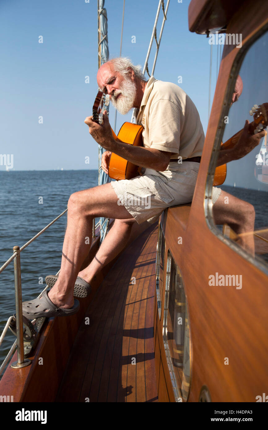 Older man on his sailing ship plays the guitar Stock Photo