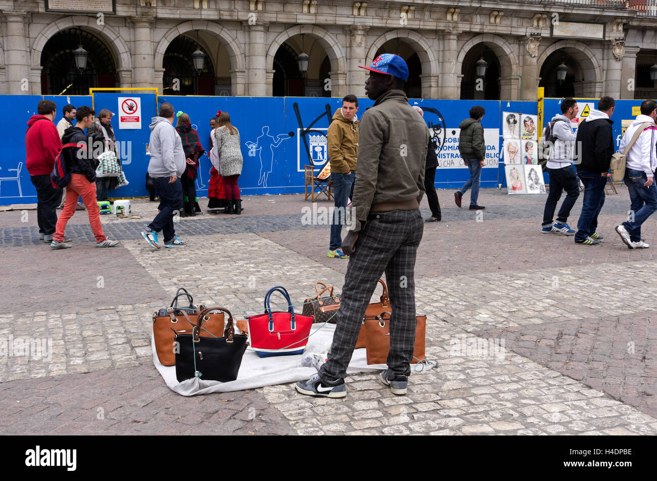 African vendors, standing by purse display (watching for police) in Plaza Mayor. Stock Photo