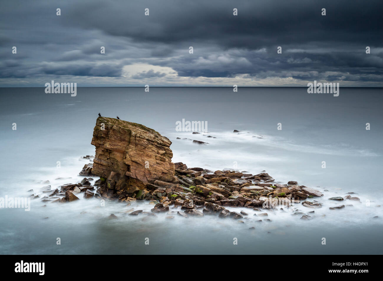 Lone sea stack at Charlie's Garden, Northumberland, after sun set and with the North Sea at high tide with a cold, moody sky Stock Photo