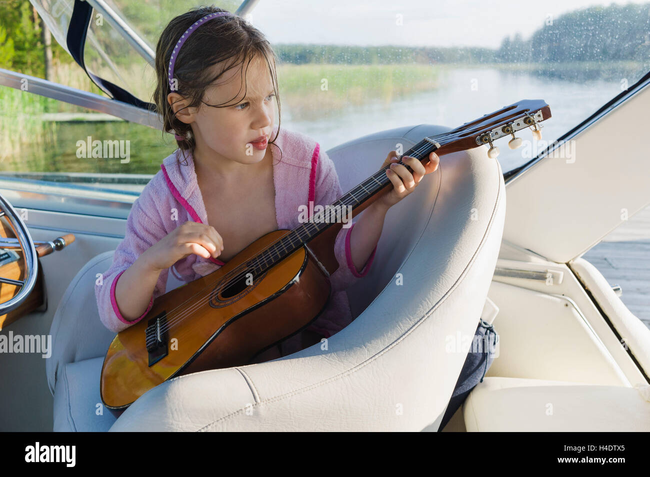 Girls in pink bathrobe sit on a boat and plays the guitar Stock Photo
