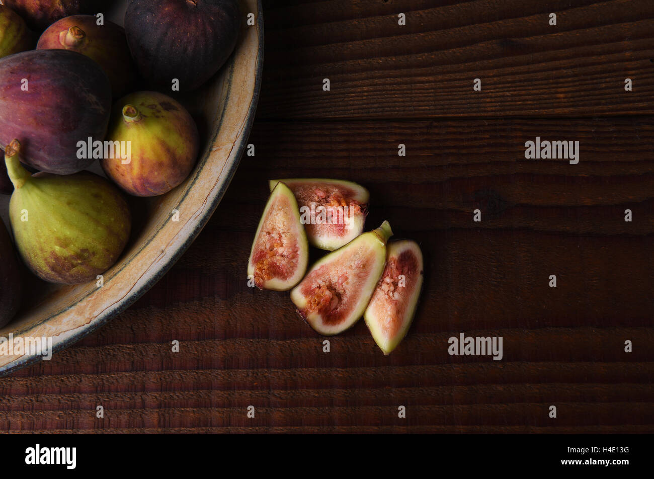 A plate full of fresh figs with one cut up on a dark wood table. Stock Photo
